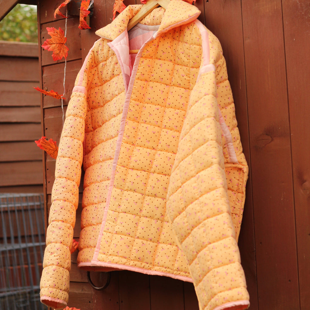 Orange quilted jacket hanging on a clothesline with autumn leaves against a wooden shed background.