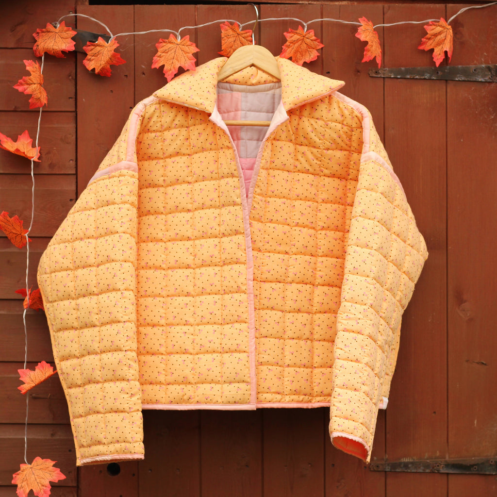 Orange quilted jacket hanging on a wooden shed with autumn leaves.