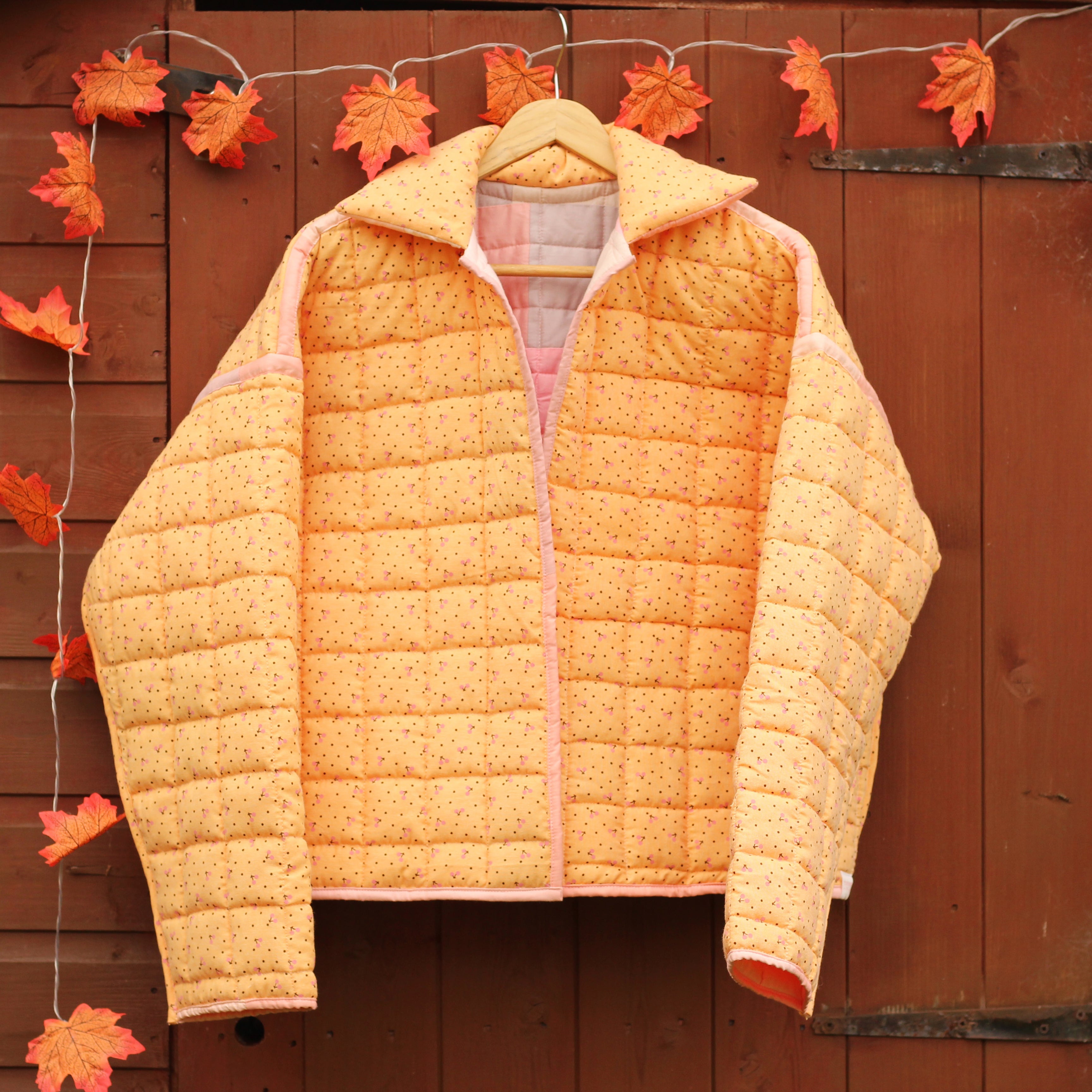 Orange quilted jacket hanging on a wooden shed with autumn leaves.
