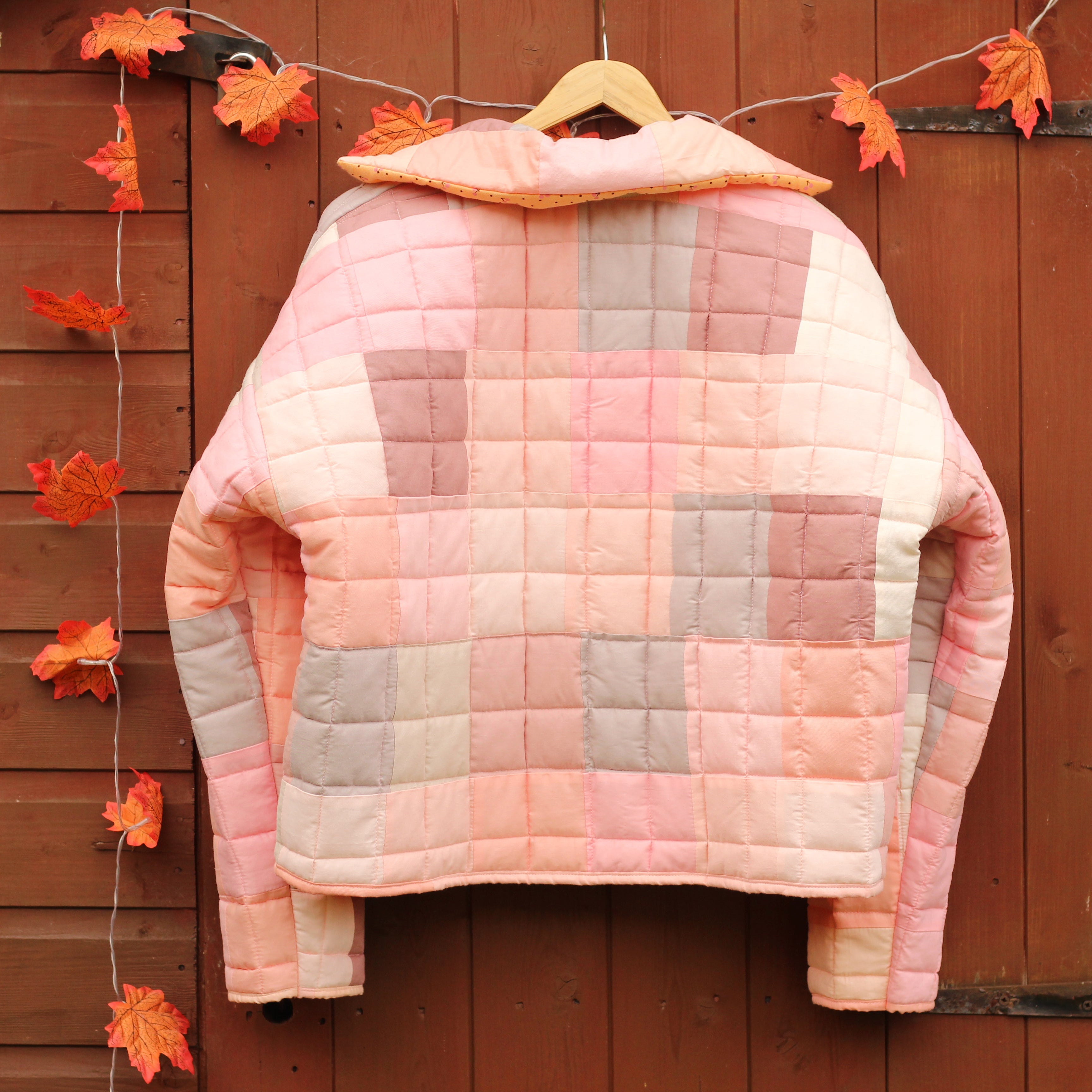 Quilted jacket with a checkered pattern hanging on a wooden wall with autumn leaves.